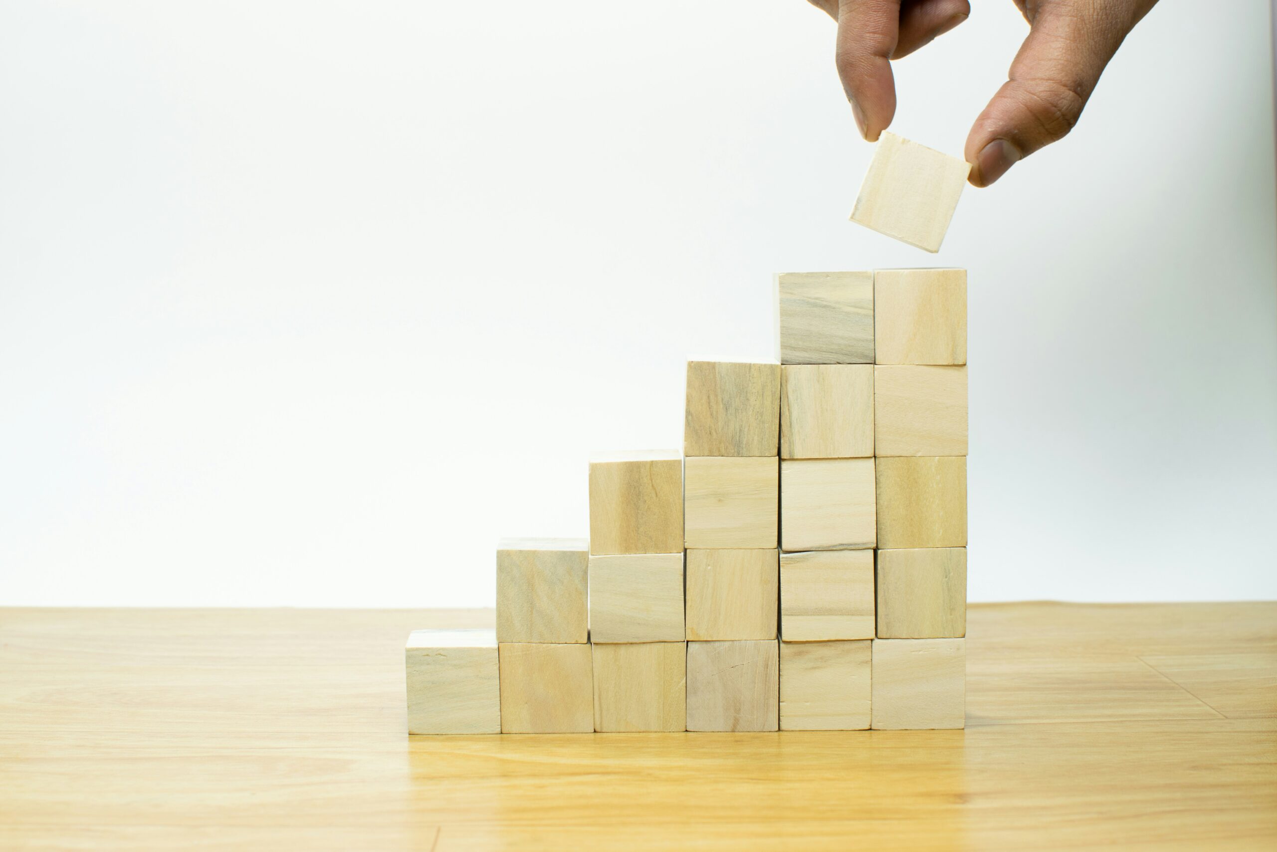 Hand placing the final wooden block on top of a staircase made from stacked cubes, symbolizing growth and team building.