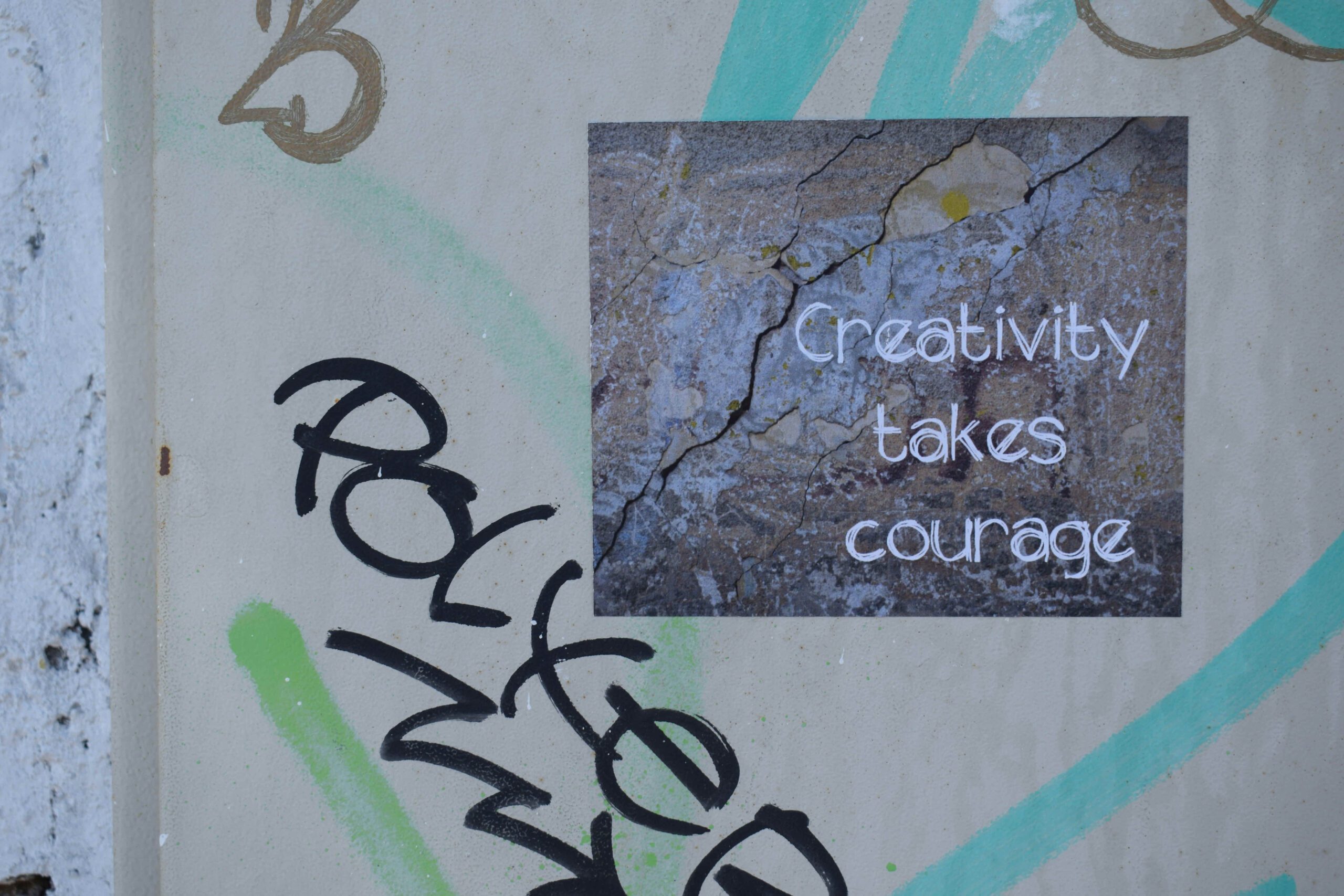 Graffiti wall with a weathered poster reading “Creativity takes courage,” symbolizing creative operations and leadership mindset.