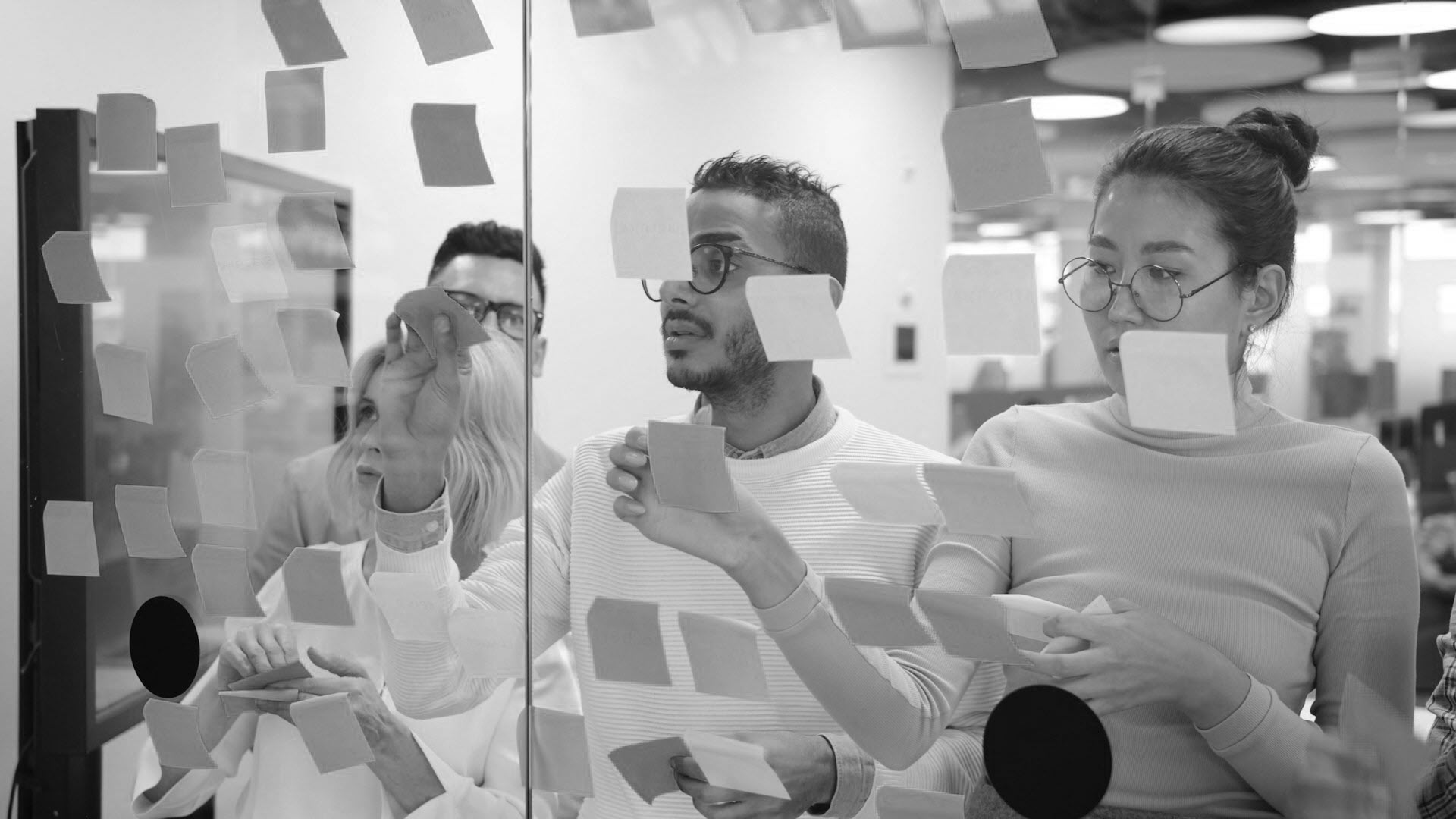 Creative team collaborating in an office, placing sticky notes on a glass wall during a strategy and brainstorming session.